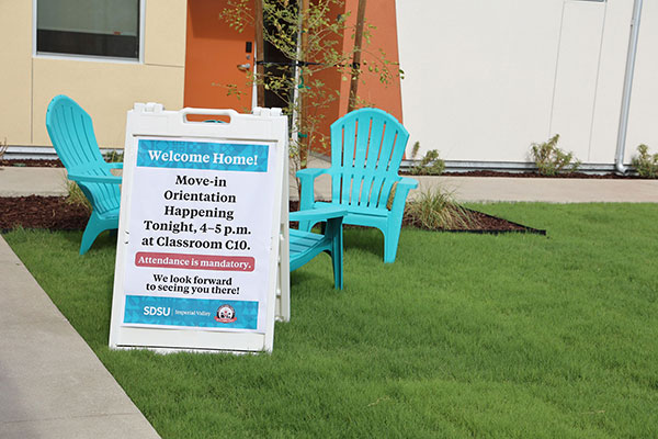 A campus lawn with turquoise outdoor chairs and a welcome sign directing students to move-in orientation at Classroom C10.