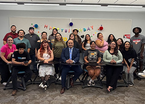 A diverse group of students and staff pose for a group photo in a classroom with a Happy Birthday banner.
